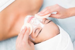 Upward view of hands cleaning woman face with sponge at spa center